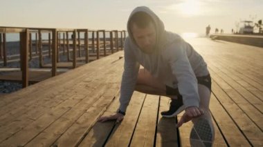 Genç adam gün doğumu açık havada egzersiz sırasında bacağını germe