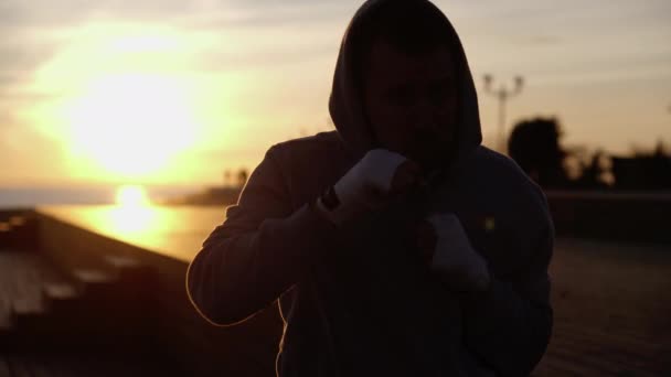 Чоловік тренує удари для боїв на відкритому повітрі ввечері, перед камерою — стокове відео