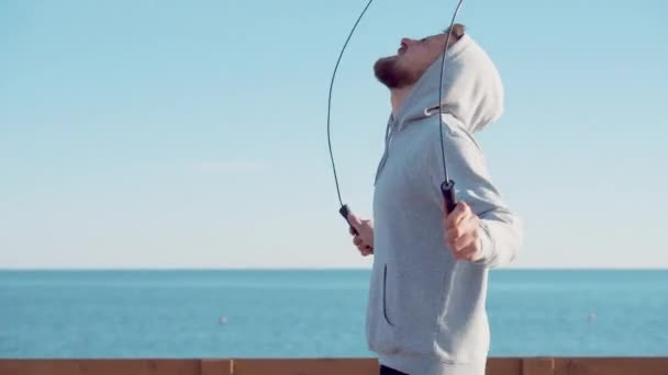 Чоловік стрибає мотузкою проти моря і неба — стокове відео