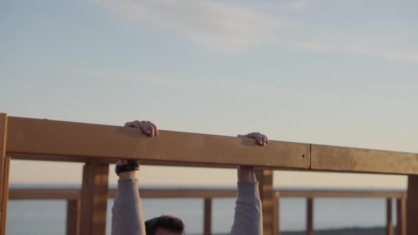 Homem está puxando para cima na barra transversal ao ar livre área de esporte perto do mar — Vídeo de Stock