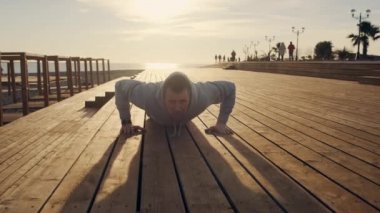 Erkek atlet güneşli bir akşamda denize yakın şehir seti üzerinde push upyapıyor