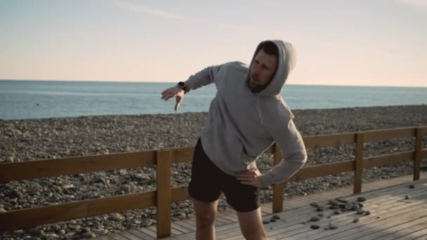 Спортсмен робить плитки торсу і розтягує руки на морському узбережжі — стокове відео