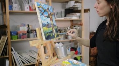 Kadın sanatçı ağaç ve dağların manzara ile resim üzerinde çalışıyor