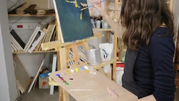 Женщина делает эскиз изображения кистью и красками на черном холсте — стоковое видео