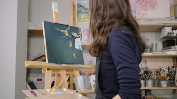 Stüdyoda çalışan sanatçı kadının arkasından görünüm, boyalar tarafından bir resim boyama — Stok video