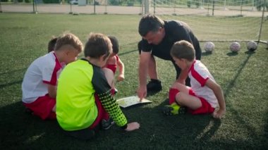 Antrenör küçük erkek futbolcular için futbol sahası planı gösteriyor