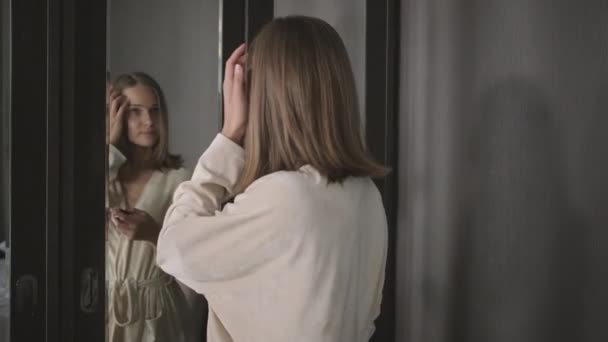 Mulher está olhando para o espelho e corrigindo seu penteado — Vídeo de Stock