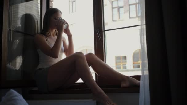 Sonriente dama gustos café sentado en el alféizar de la ventana en el día libre — Vídeos de Stock