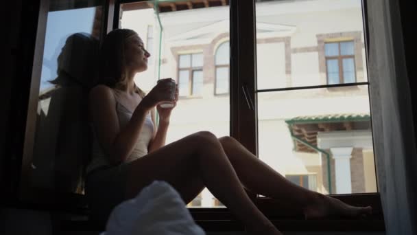 Pieds nus dame assis sur le rebord de la fenêtre et boit du café — Video