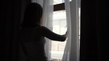 Kadın perdeleri hareket ettiren ve pencereyi açan, sokağa bakan