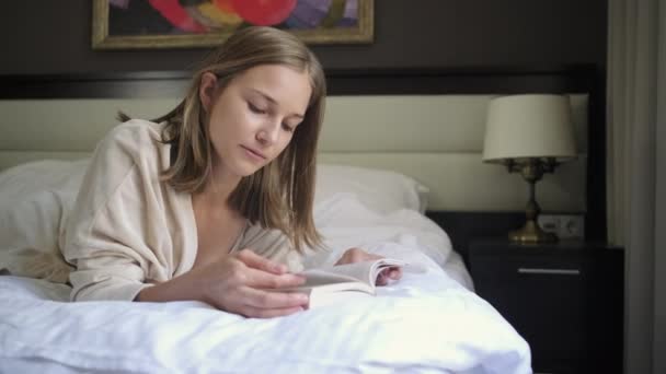 Η γυναίκα διαβάζει το βιβλίο ξαπλωμένο στο κρεβάτι στο σπίτι — Αρχείο Βίντεο