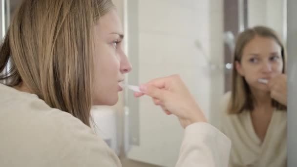 Junge Frau putzt im Spiegel reflektierende Zähne — Stockvideo