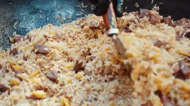 Cook mixes pilaf with ladle in caldron at food festival — Stock Video