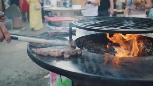 Person bewegt Fleischscheiben mit Zange gegen Grillfest — Stockvideo