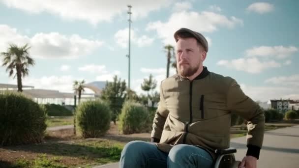 Впевнений бородатий чоловік їде на інвалідному візку на відкритому повітрі один в сонячний день — стокове відео