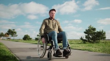 Tekerlekli sandalyedeki erkek hasta sıcak güneşli havalarda park alanında yürüyor