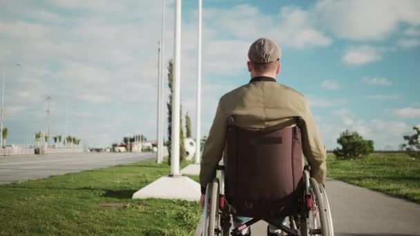 Homme en fauteuil roulant se déplace seul dans la rue, roues tournantes, vue arrière — Video