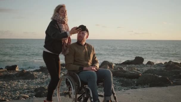 男性の車椅子ユーザーと彼の女性の友人は、スマートフォンで自分撮りを取っています — ストック動画