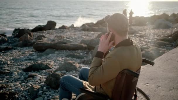 Gehandicapte man praat op mobiel aan de kust — Stockvideo