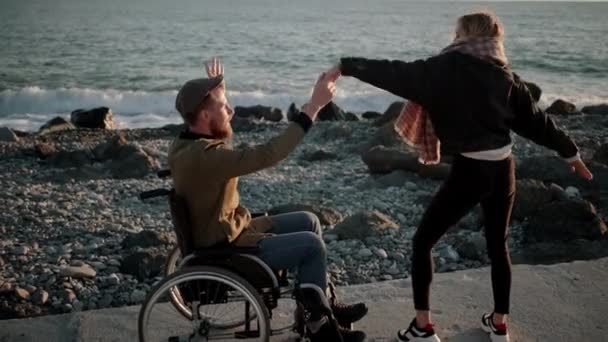 Drôle de jeunes gens dansent près de la mer, homme en fauteuil roulant utilisateur et jeune dame — Video