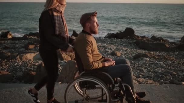 Vrouw het verzorgen van gehandicapte man en wandelen met hem door de zee — Stockvideo