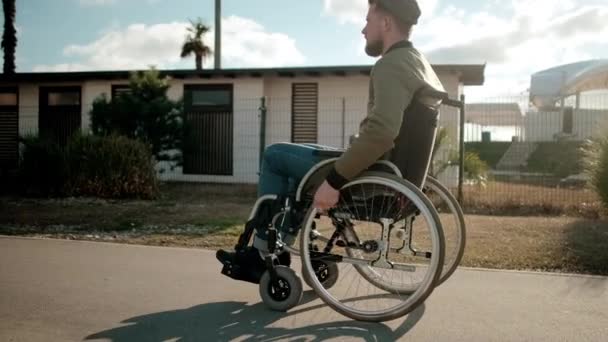 Jovem com pernas paralisadas em cadeira de rodas está andando sozinho nas ruas da cidade — Vídeo de Stock