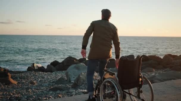 Man is standing up from invalid carriage on sea shore, lifting hands, rejoicing — Stock Video