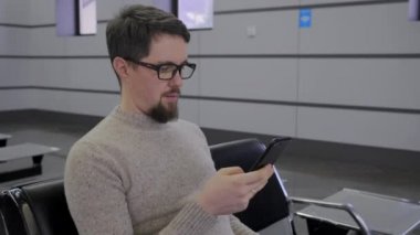 Gözlüklü adam bekleme odasında akıllı telefondan konuşuyor.