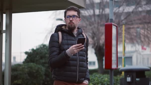 Ciudadano espera autobús en la parada de la celebración de teléfono inteligente — Vídeos de Stock