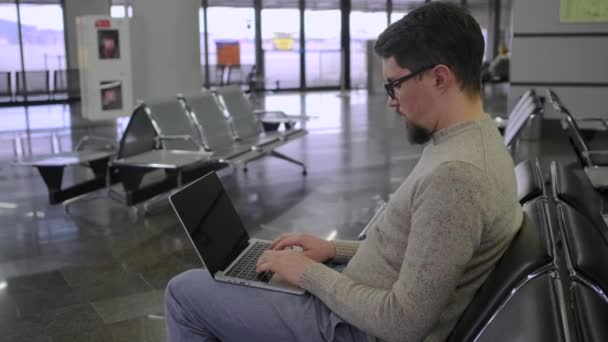 Kille typer på laptop sitter i tomma väntrum — Stockvideo