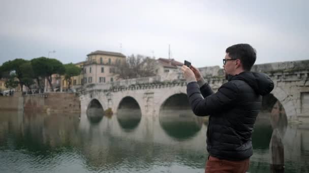 Kille turist filmer gamla bron reflekterar i floden — Stockvideo