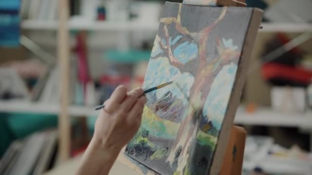 Женщина рисует пейзаж на холсте акриловыми красками в студии — стоковое видео