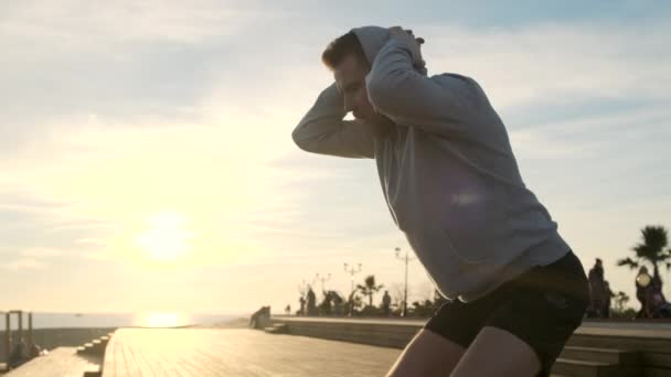 Человек тренируется на закате и делает приседания — стоковое видео