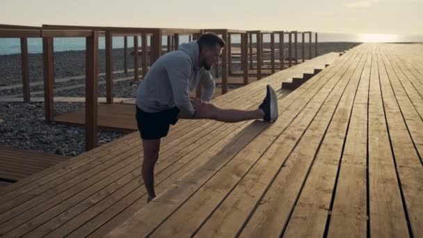 Homem aquecendo com perna esticar exercício ao ar livre ao pôr do sol — Vídeo de Stock