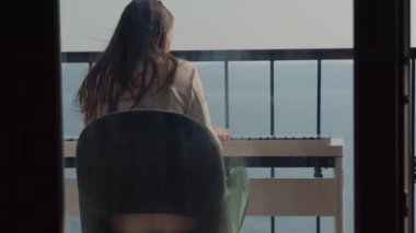 Kadın dairenin balkonunda elektronik piyano çalıyor.