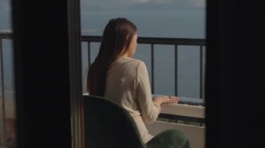 Genç ve narin bir dişi, denizin üstündeki balkonda piyano çalıyor.