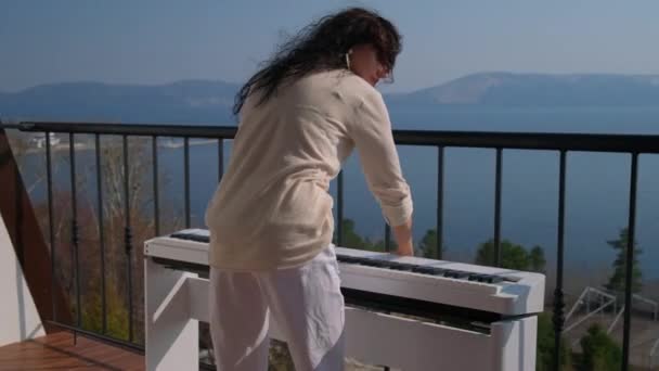 Женщина устанавливает цифровое фортепиано на балконе квартиры — стоковое видео