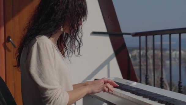 Жінка практикує грати на цифровому піаніно на балконі — стокове відео