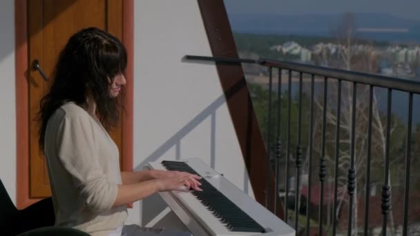 Woman is learning play music by electronic piano at balcony — Stock Video