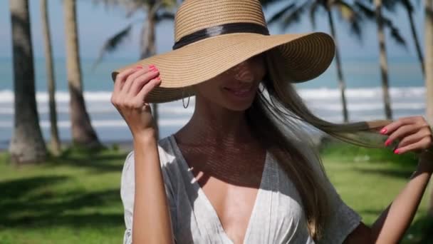 Mujer rubia con sombrero dando un paseo bajo las palmeras — Vídeo de stock