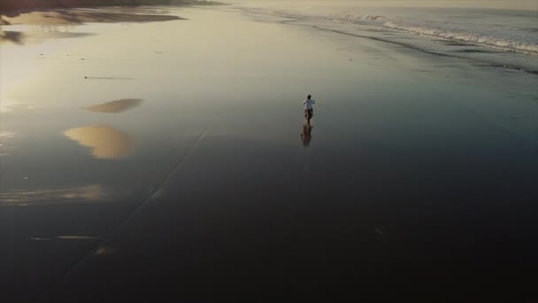 Повітряний постріл людини на велосипеді, що їде по лінії серфінгу тропічного океану в сутінках — стокове відео