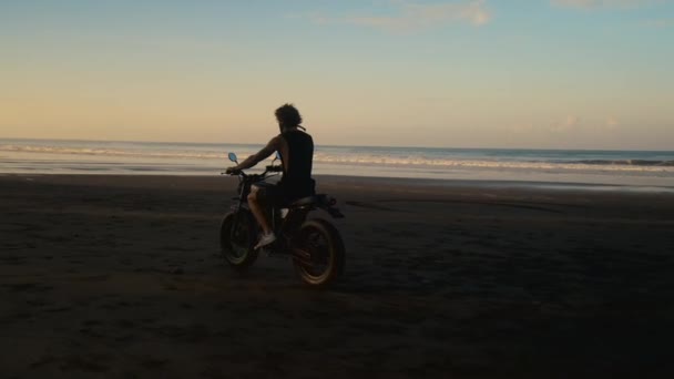 Motorcyklist rider på svart sandstrand vid solnedgången — Stockvideo