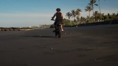 Turist okyanus kıyısında motosiklet sürüyor.