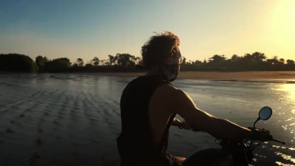 Motociclista está montando en la costa del océano al atardecer — Vídeos de Stock
