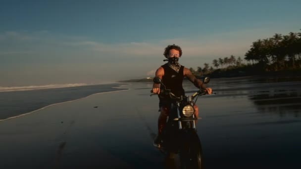 Lonely rider drives a bike at the ocean beach at sunset — Stock Video