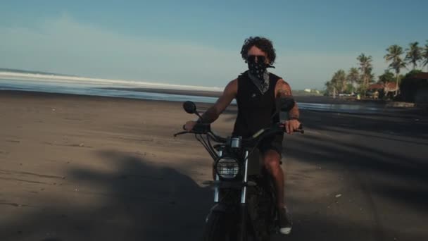 Человек поворачивает легкий велосипед вокруг на берегу океана — стоковое видео