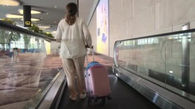 Tekerlekli bavullu bir kadın turist travelatöre biniyor.