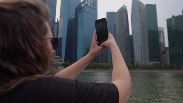 Vrouw is het nemen van foto en video met de smartphone van wolkenkrabbers — Stockvideo