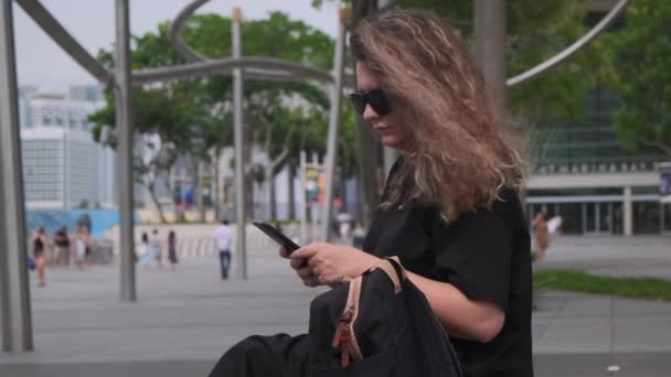 Jonge vrouw houdend rust met mobiel na stadswandeling — Stockvideo