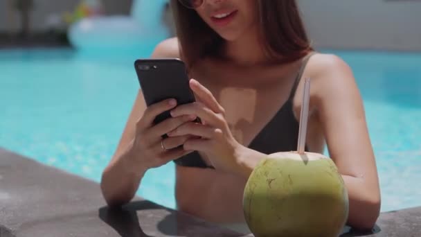 热带度假快乐的年轻女士在游泳池里用手机 — 图库视频影像